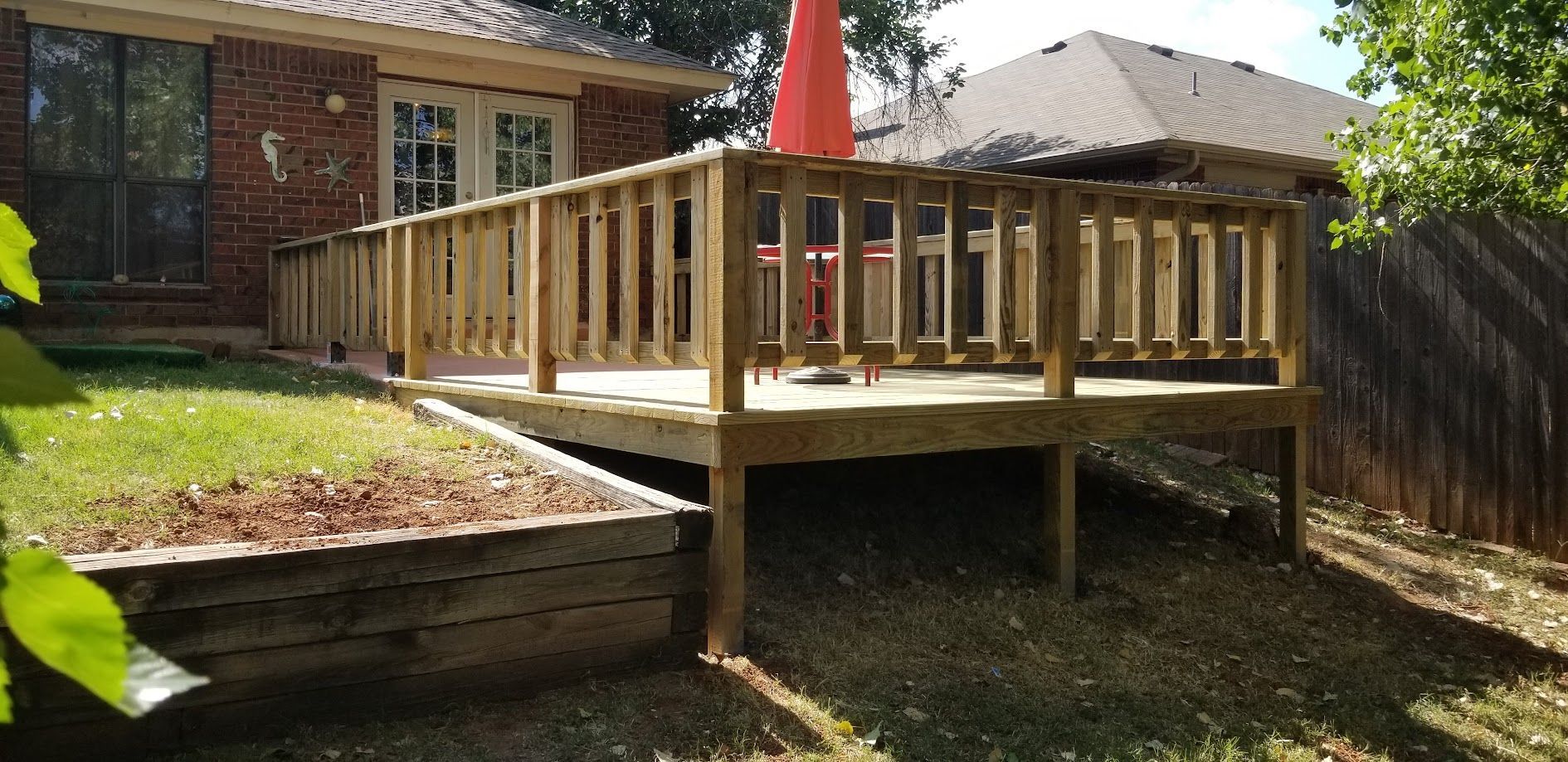 Wooden backyard deck with railing beside a brick house and a red patio umbrella