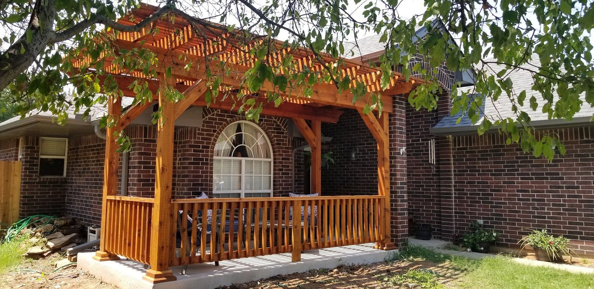 Wooden gazebo with pergola vines in a sunny backyard, framed by a brick wall and trees