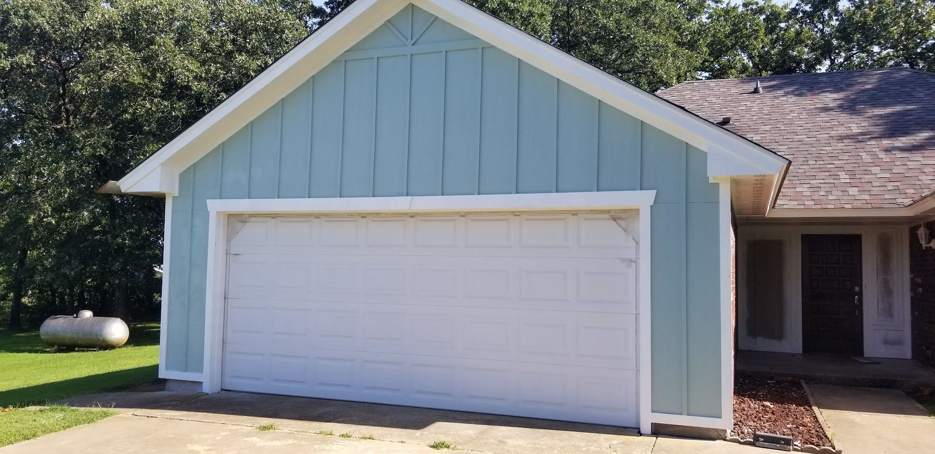 Single-story house exterior with light blue garage, white door, and front porch in sunny daylight