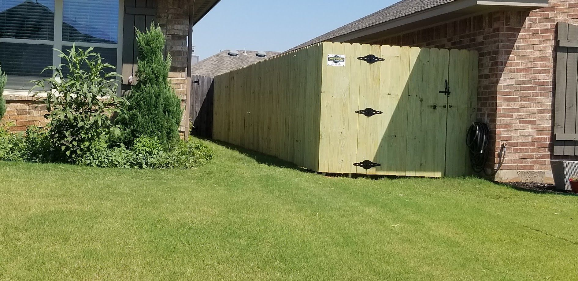 A green wooden shed beside a brick house with a grassy lawn in the foreground.