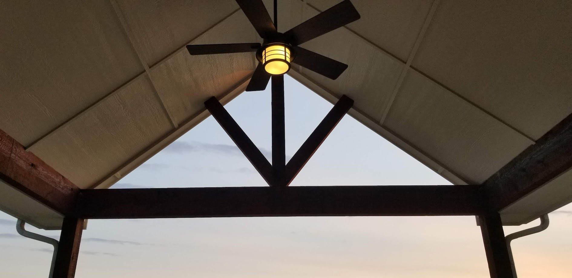 Covered patio roof with a central ceiling light and triangular truss against the evening sky
