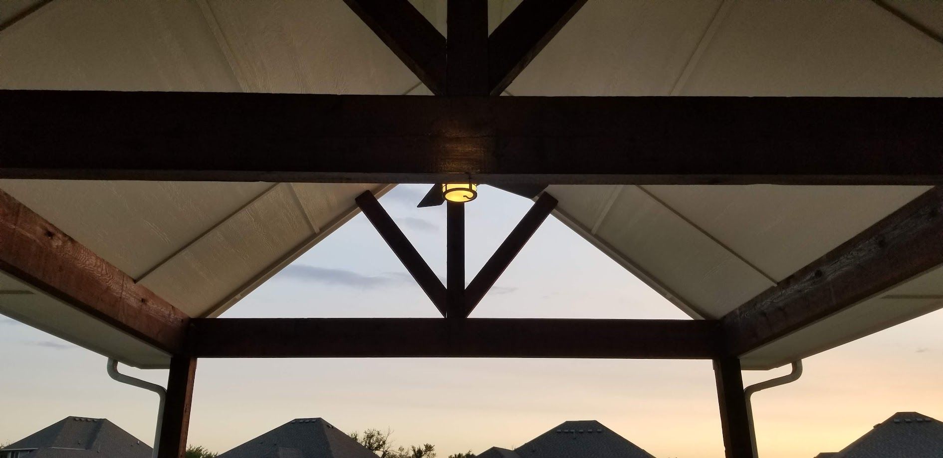 Covered pavilion roof at sunset with dark beams and mountain silhouettes in the distance