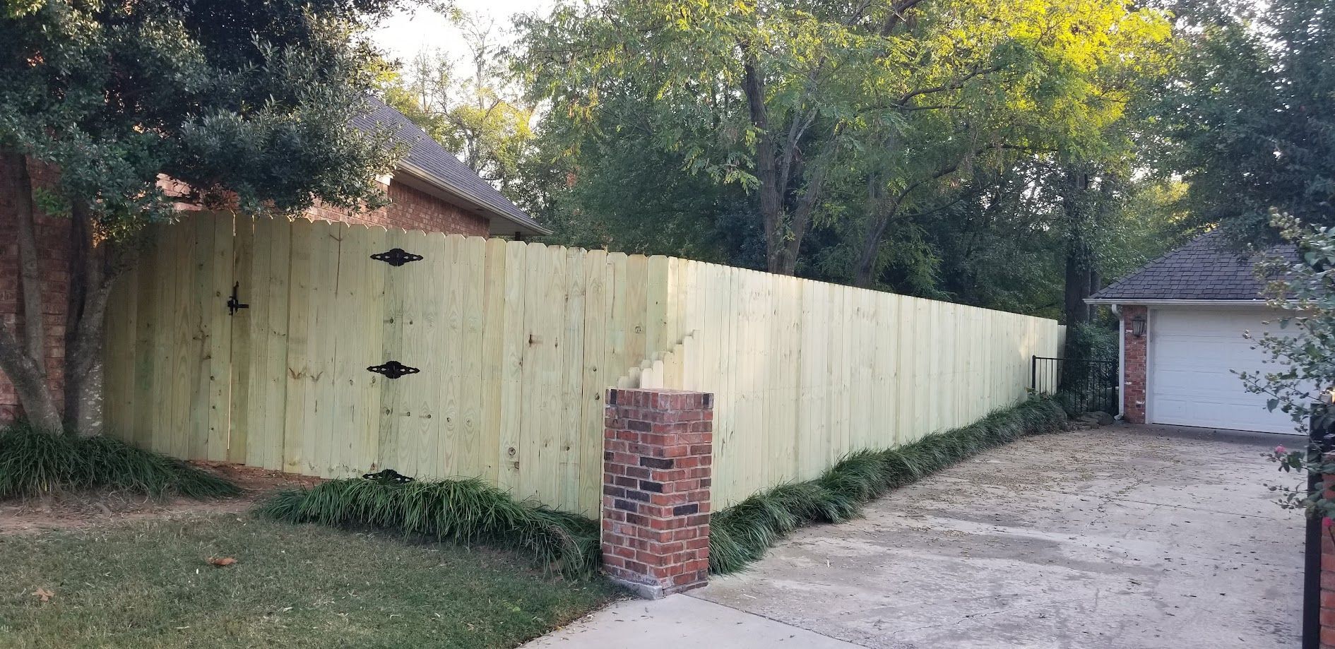 Wooden privacy fence along a driveway beside a brick mailbox and detached garage in a wooded yard