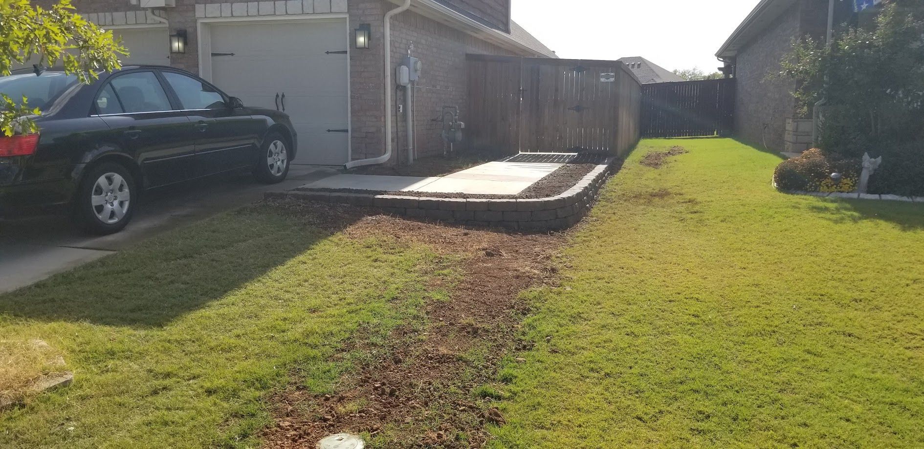 Backyard with a raised concrete patio, green lawn, and a parked black car beside a house