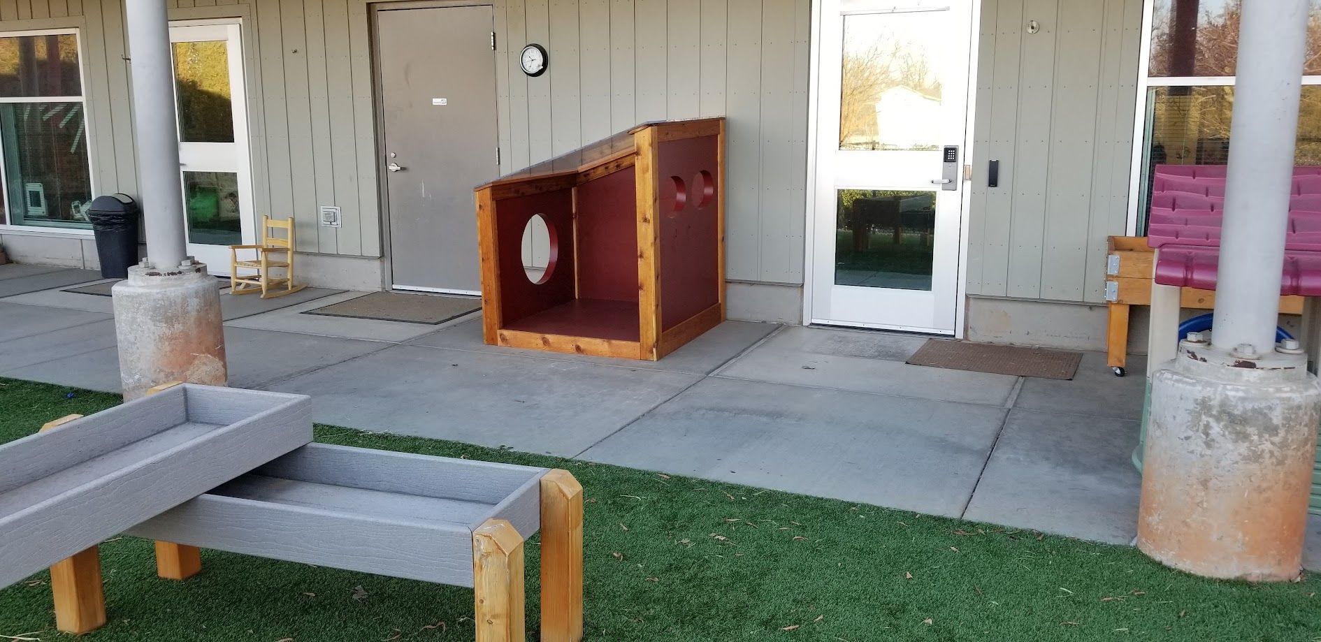 Outdoor patio with a wooden donation box, benches, and glass doors on a concrete walkway
