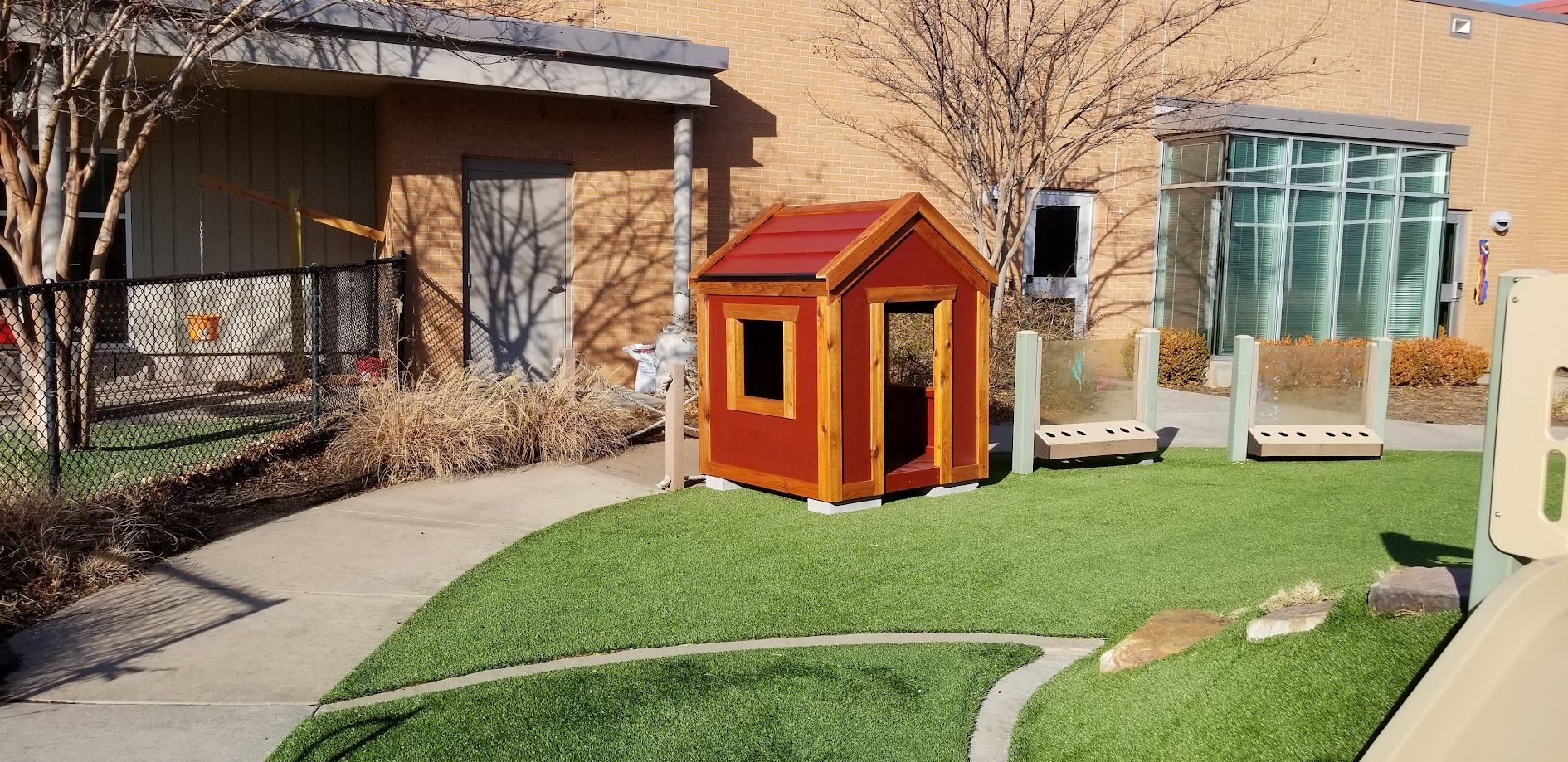 Small orange garden shed in a courtyard with grass, pathways, and a building in the background