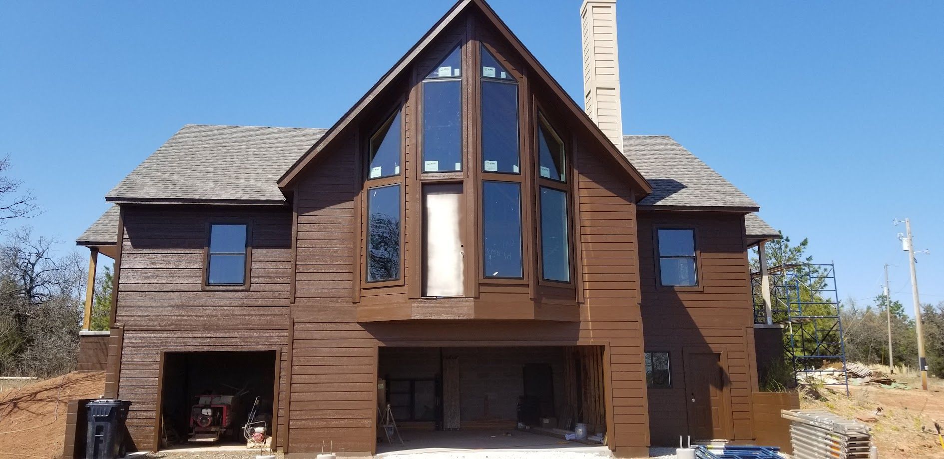 Two-story brick house under construction with large front windows and roof framing exposed