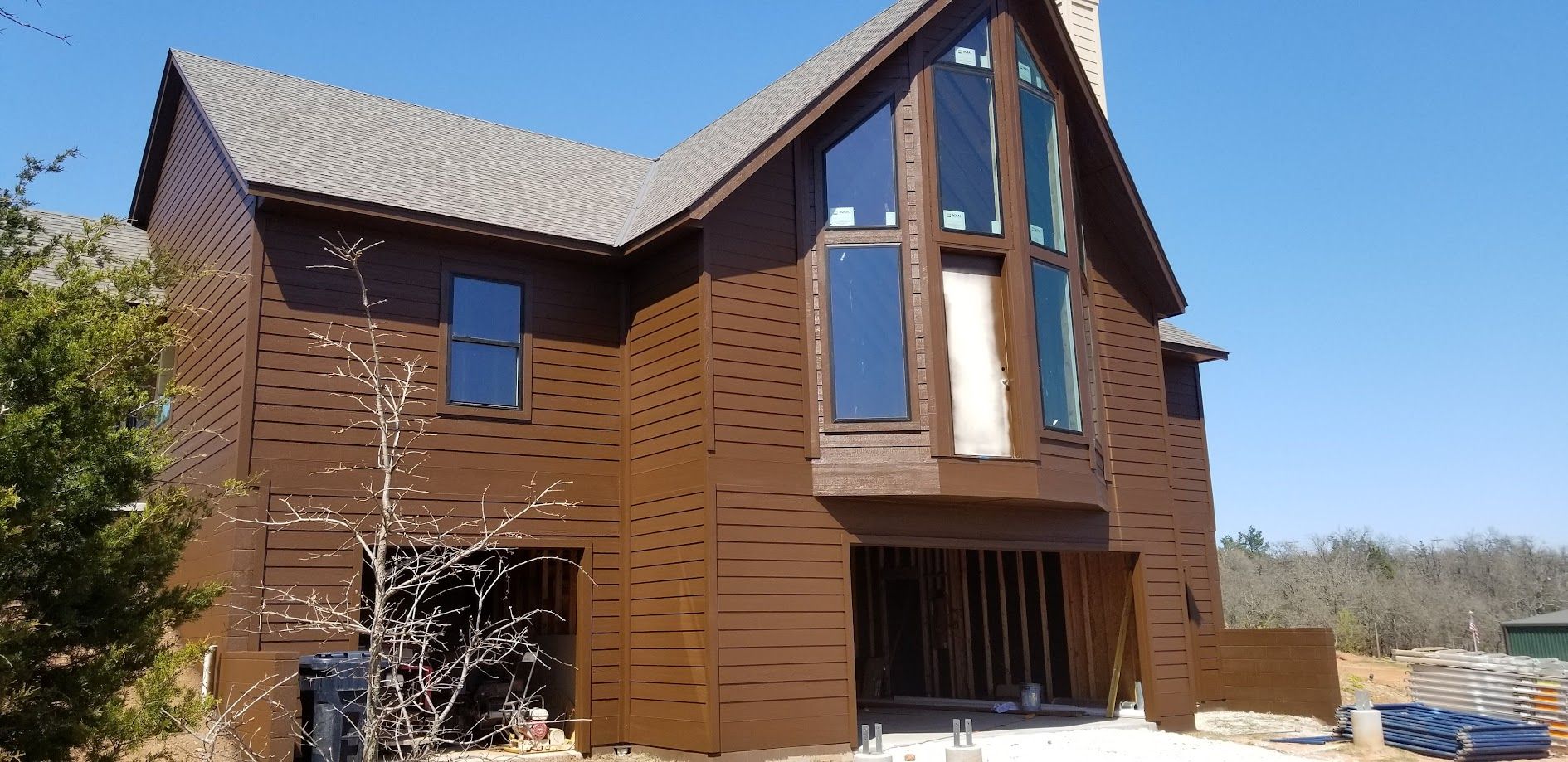 Modern brown two-story house under construction with tall central windows and a sloped roof