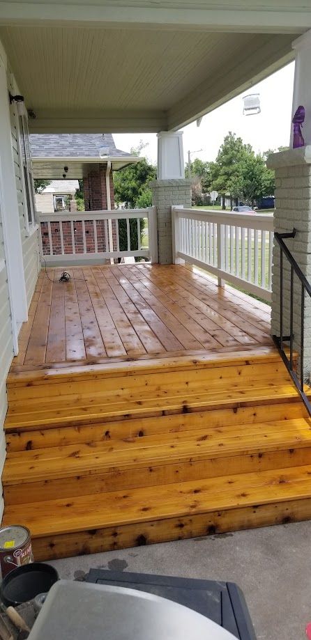 Wooden porch with steps and railing, covered roof, and wet deck boards after rain