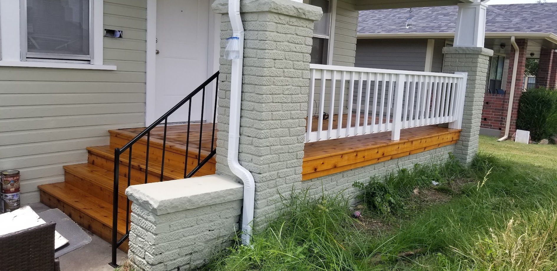Front porch with wooden steps, black railing, and white posts on a house exterior.