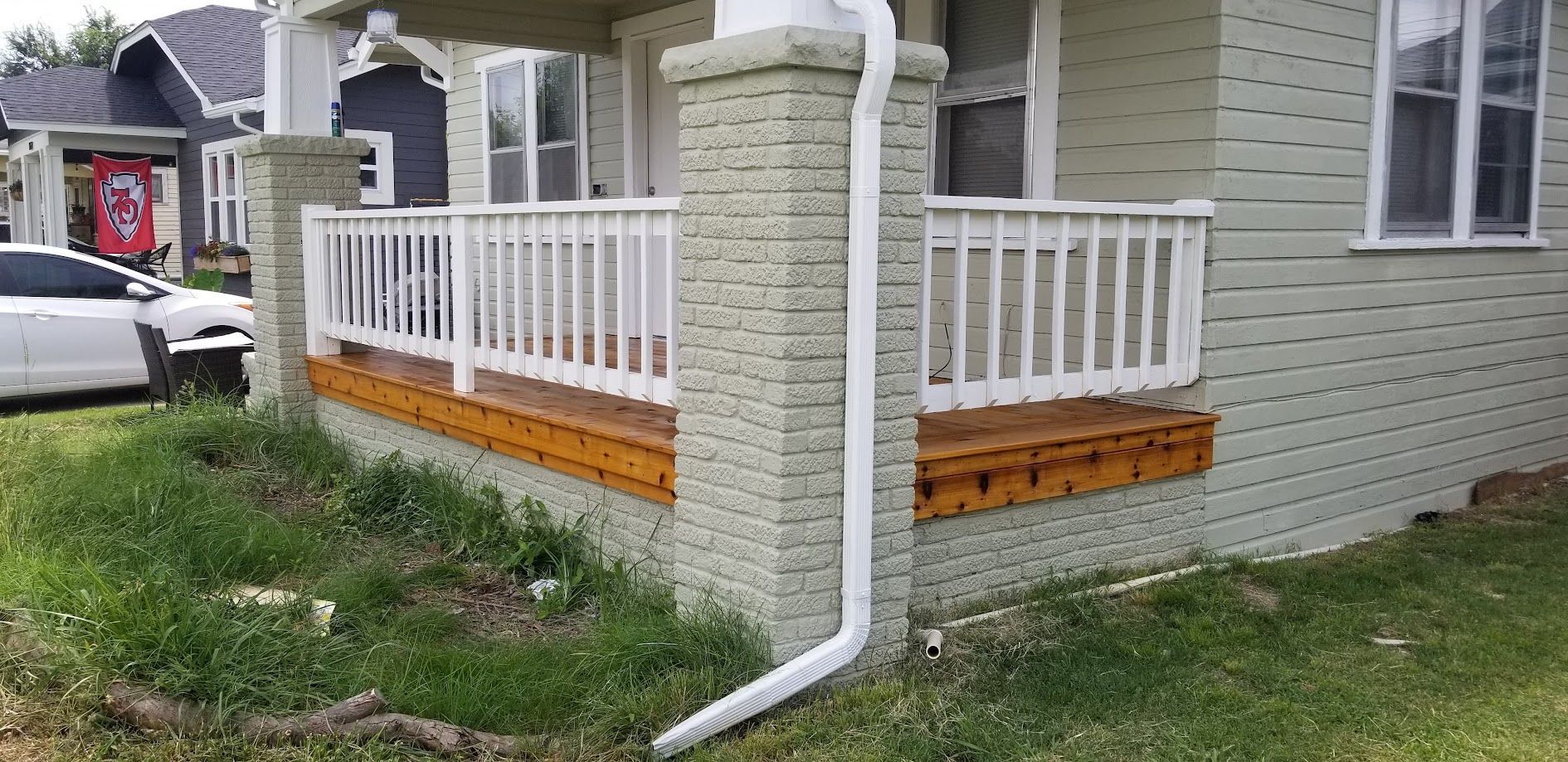 Front porch with white railing and ramp on a light gray house, with a parked car nearby.