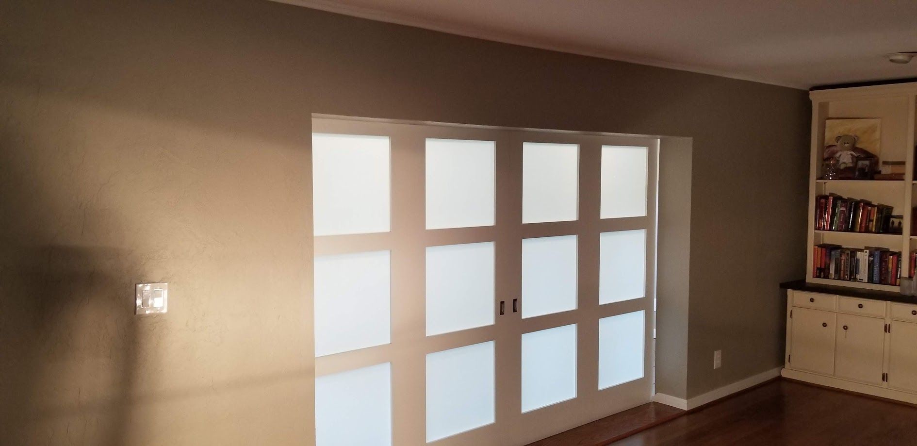 Living room with a large grid of bright windows and a built-in shelf cabinet on the right