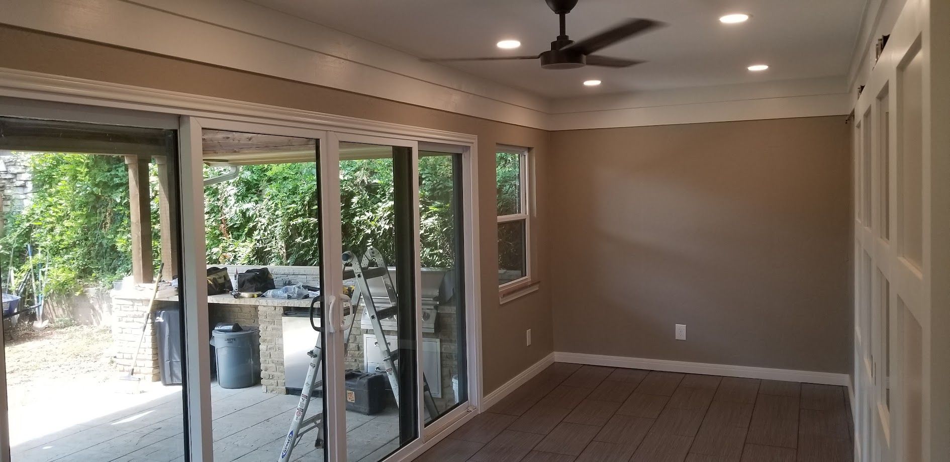 Empty sunroom with large sliding glass doors, recessed lights, ceiling fan, and wood-look floor.