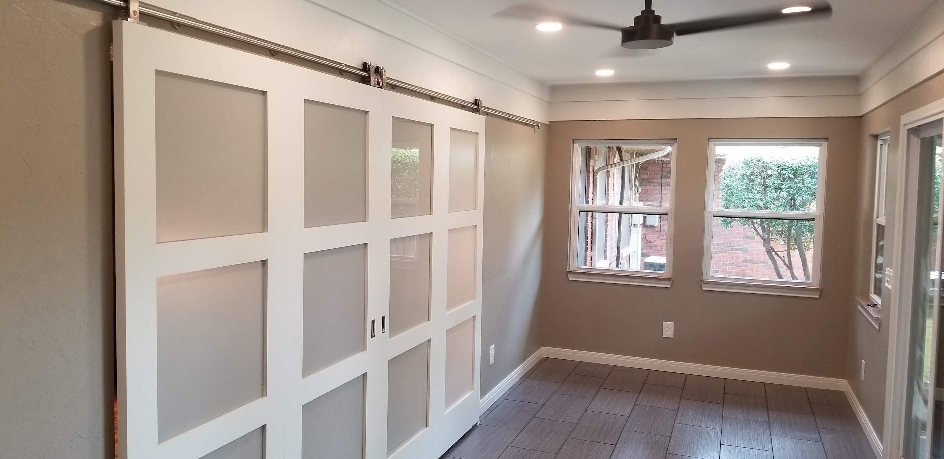 Bright sunroom with white paneled wall, ceiling fan, windows, and wood flooring