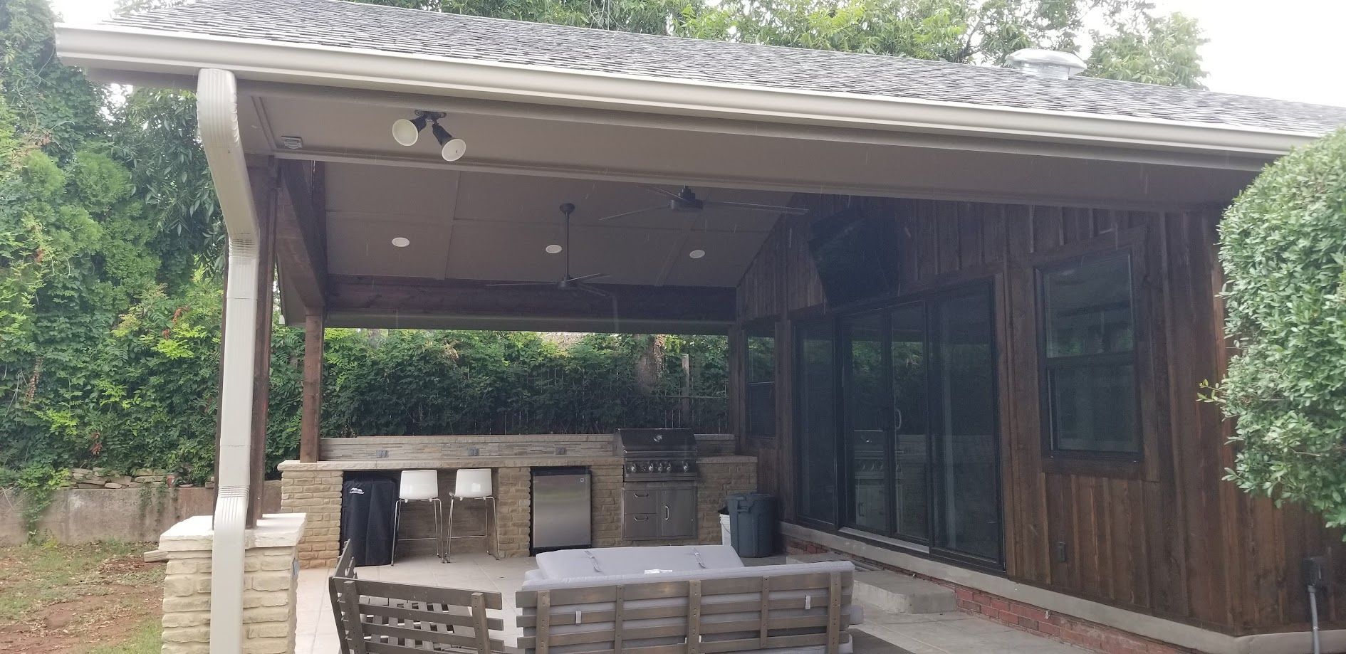 Covered outdoor patio with wooden seating, a bar counter, and sliding glass doors under a sloped roof
