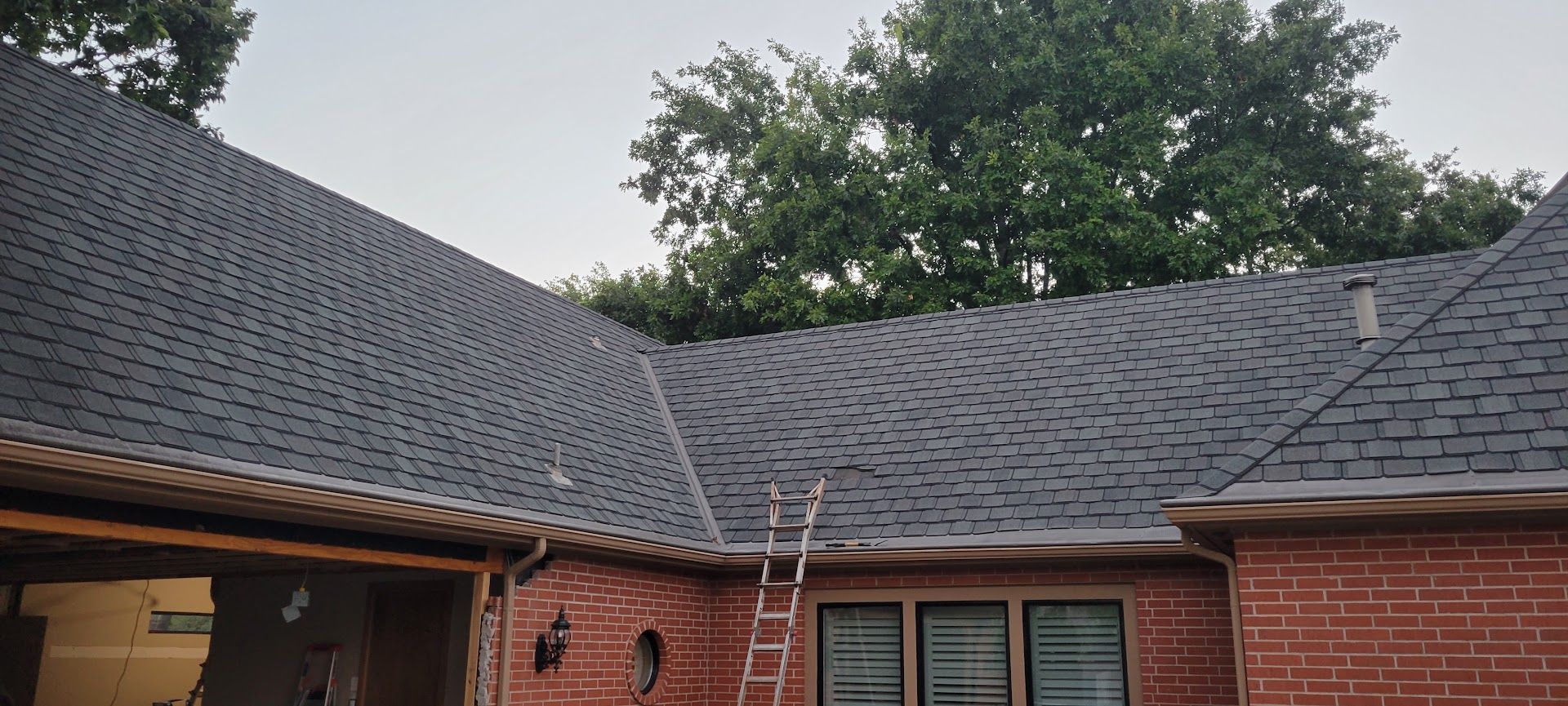 Brick house roof with dark shingles and trees in the background