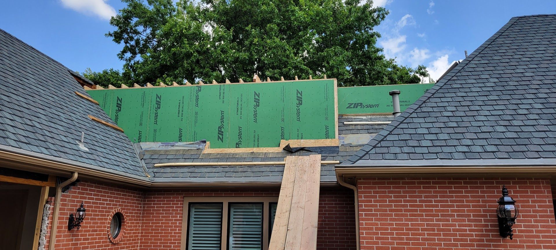 Brick house roof under repair with green sheathing and a wooden plank between dormers