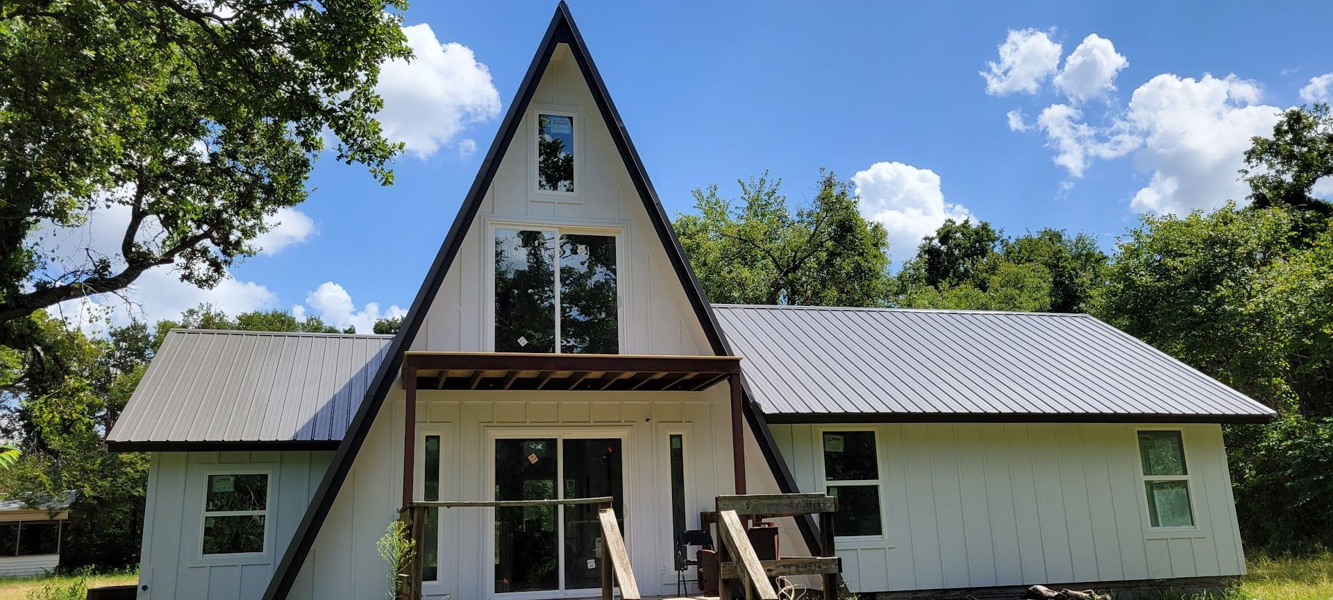 White A-frame house with a steep roof, front porch, and trees under a blue sky