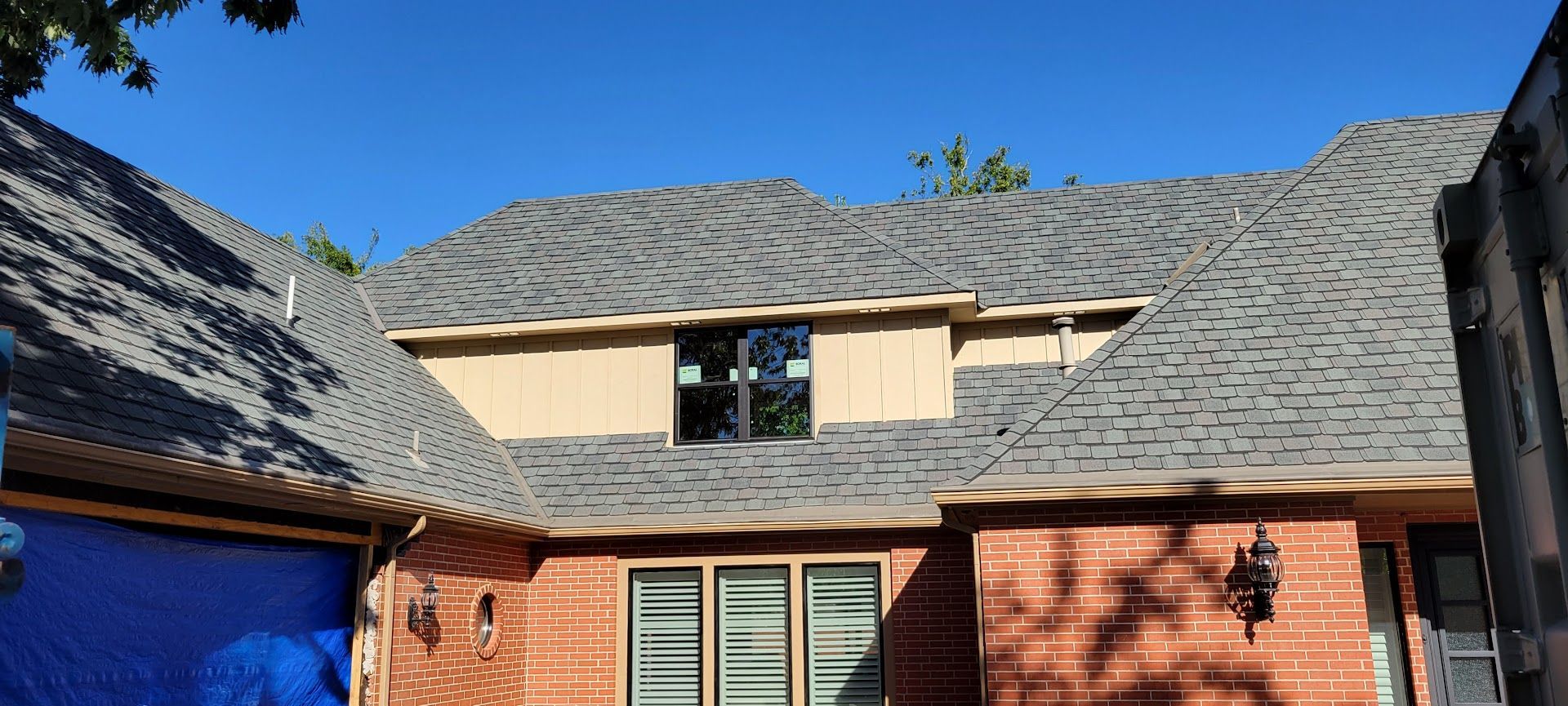 Brick house with gray shingle roof and blue sky above two dormer windows