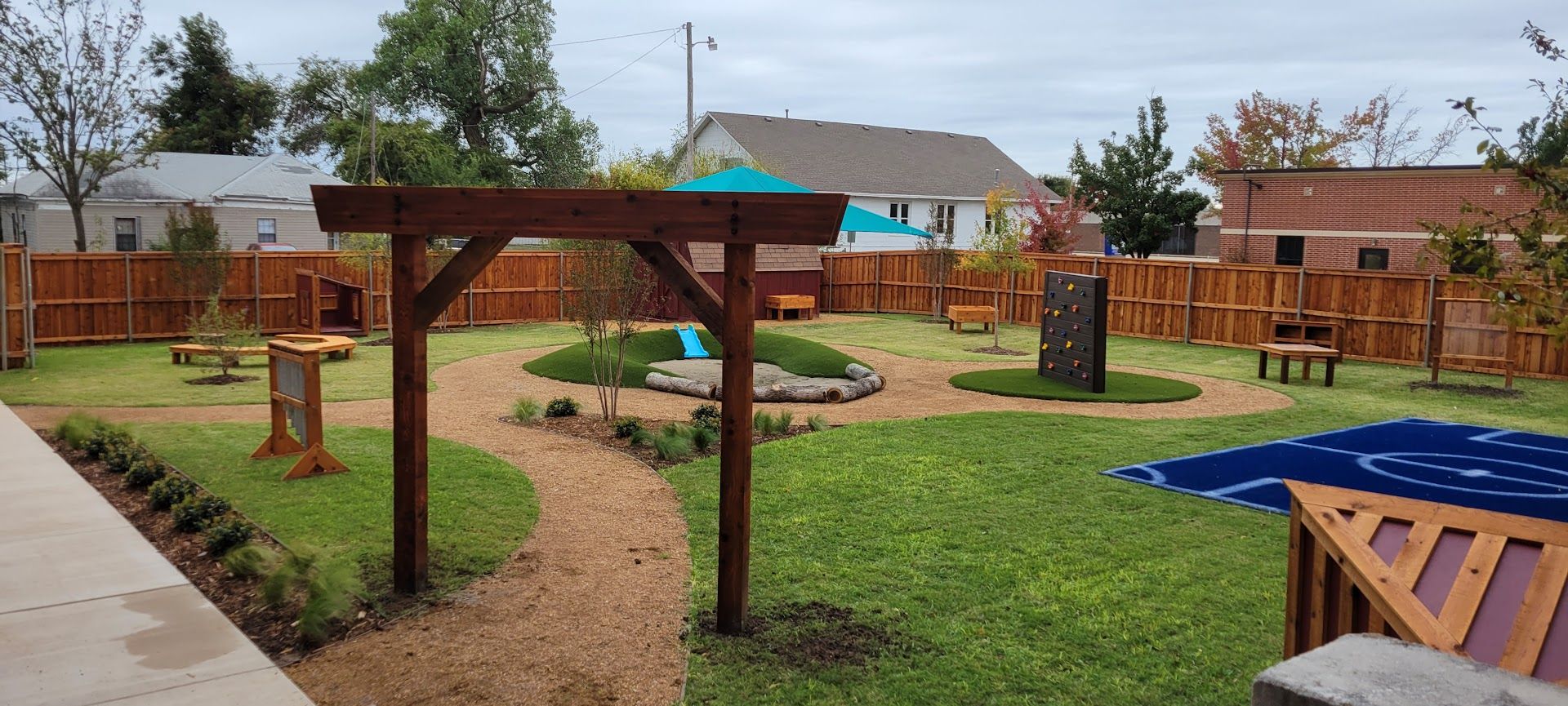 Backyard playground with wooden climbing structures, blue sandbox, and grassy lawn under cloudy skies