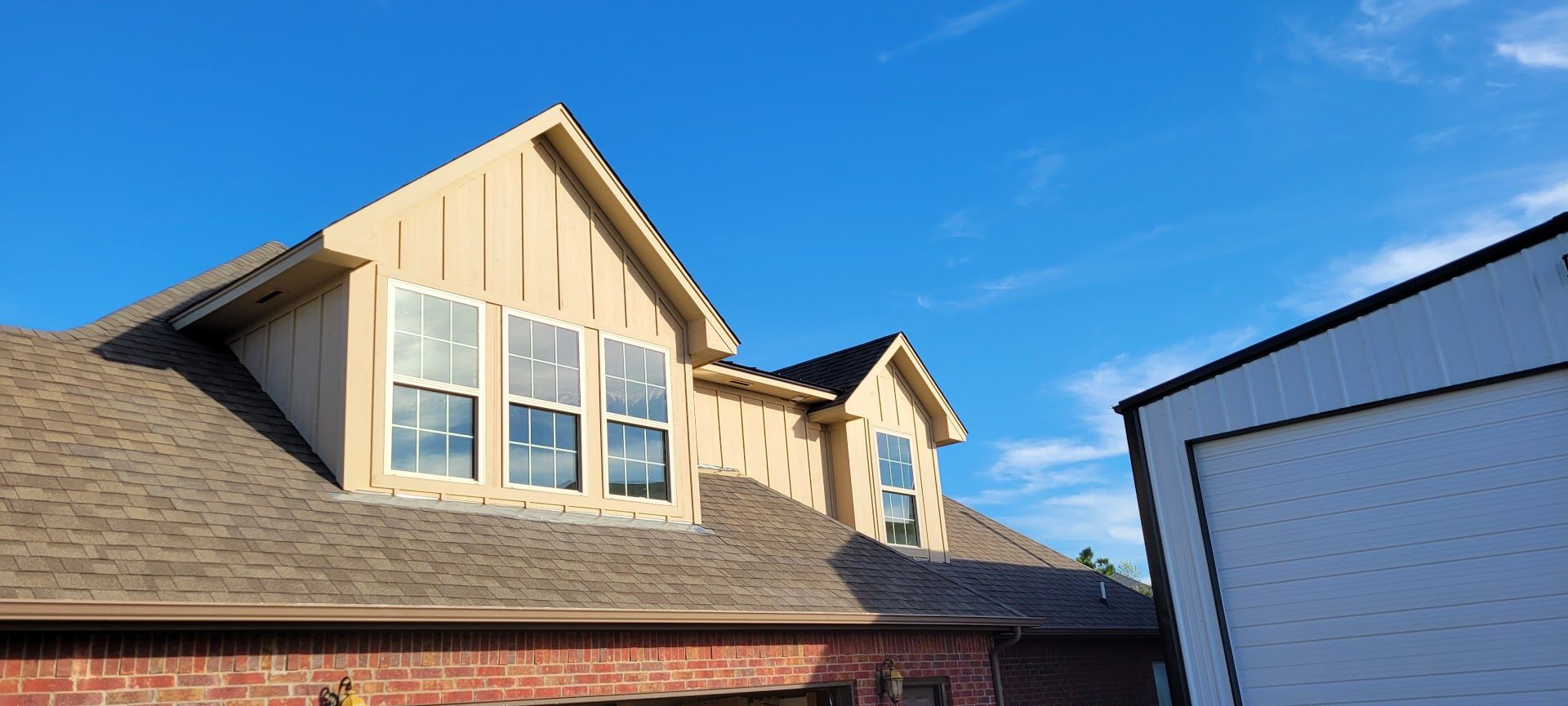 House exterior with tan gables, brick roofline, and a white garage under a blue sky