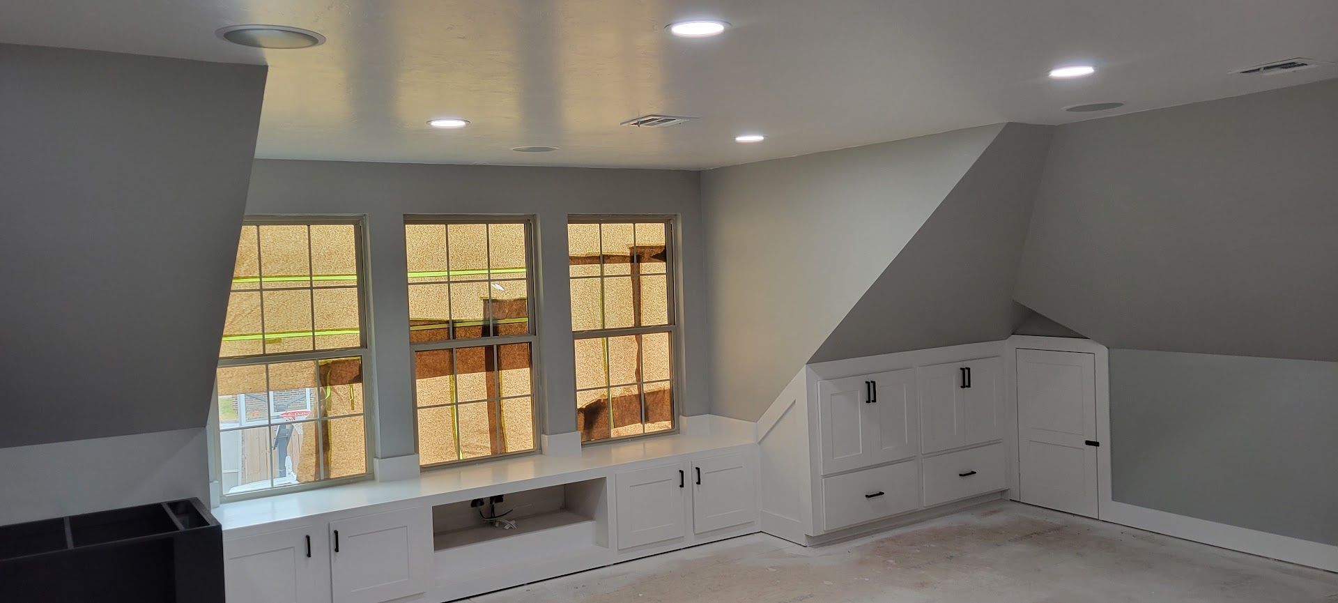 Bright empty room with gray walls, white built-in cabinets, and large windows letting in warm sunlight
