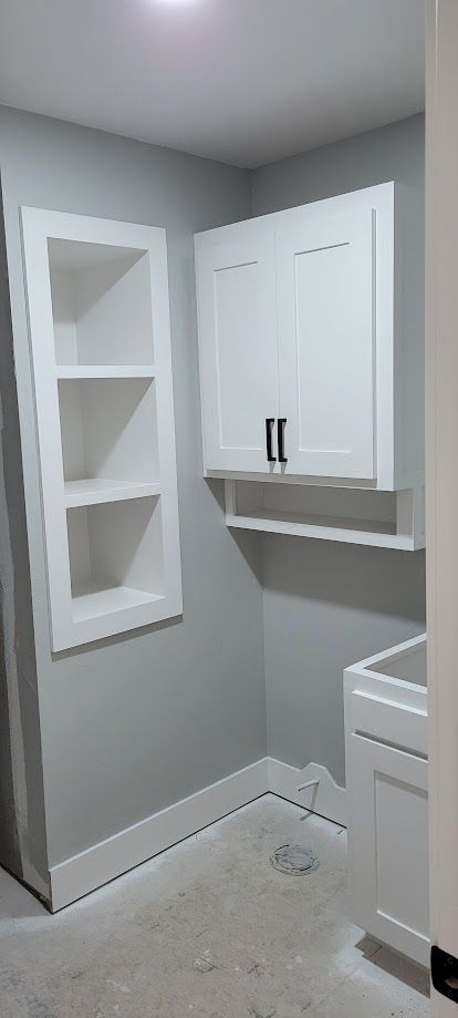 Small laundry room with white cabinets, wall shelf, and part of a washer and dryer.