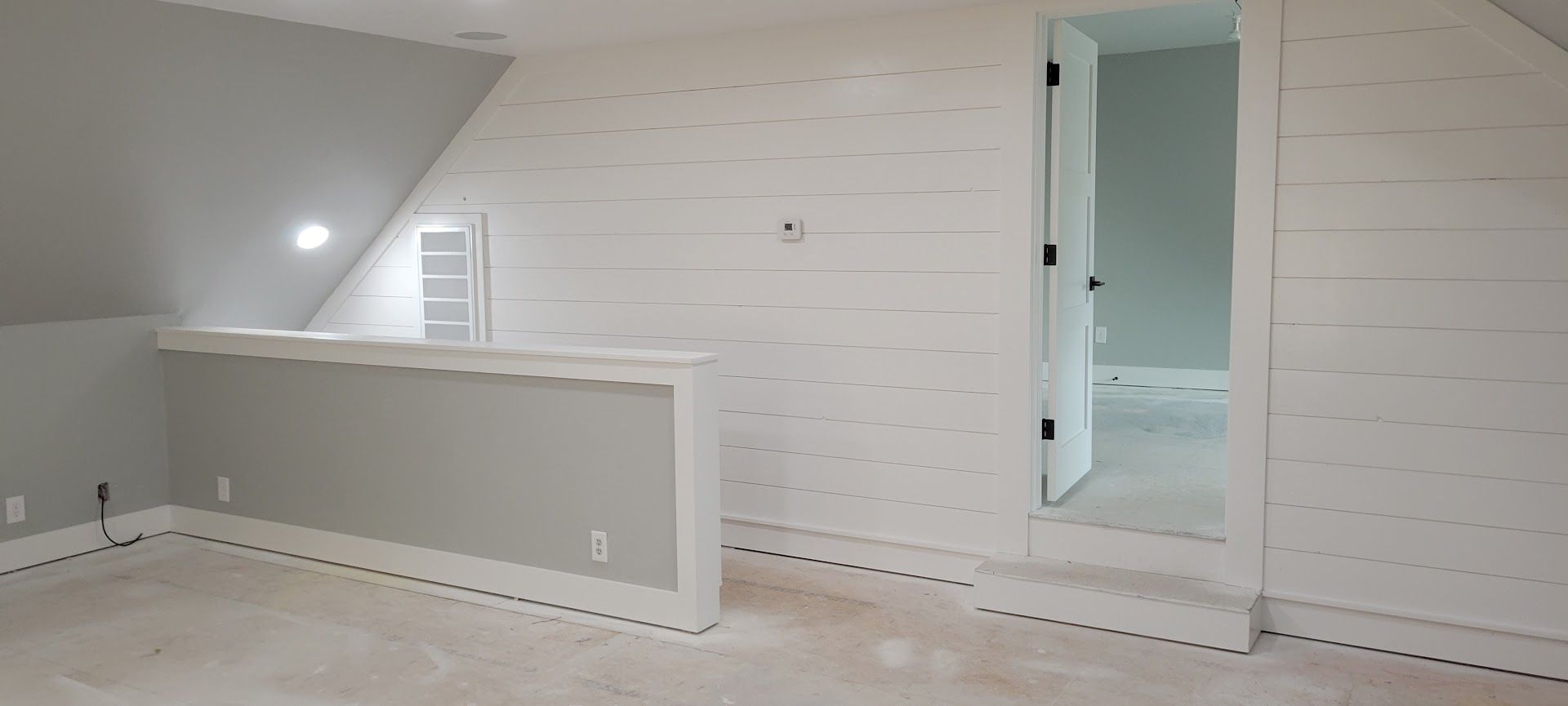 Empty white attic bedroom with sloped ceiling, striped wallpaper, and open doorway to a bathroom