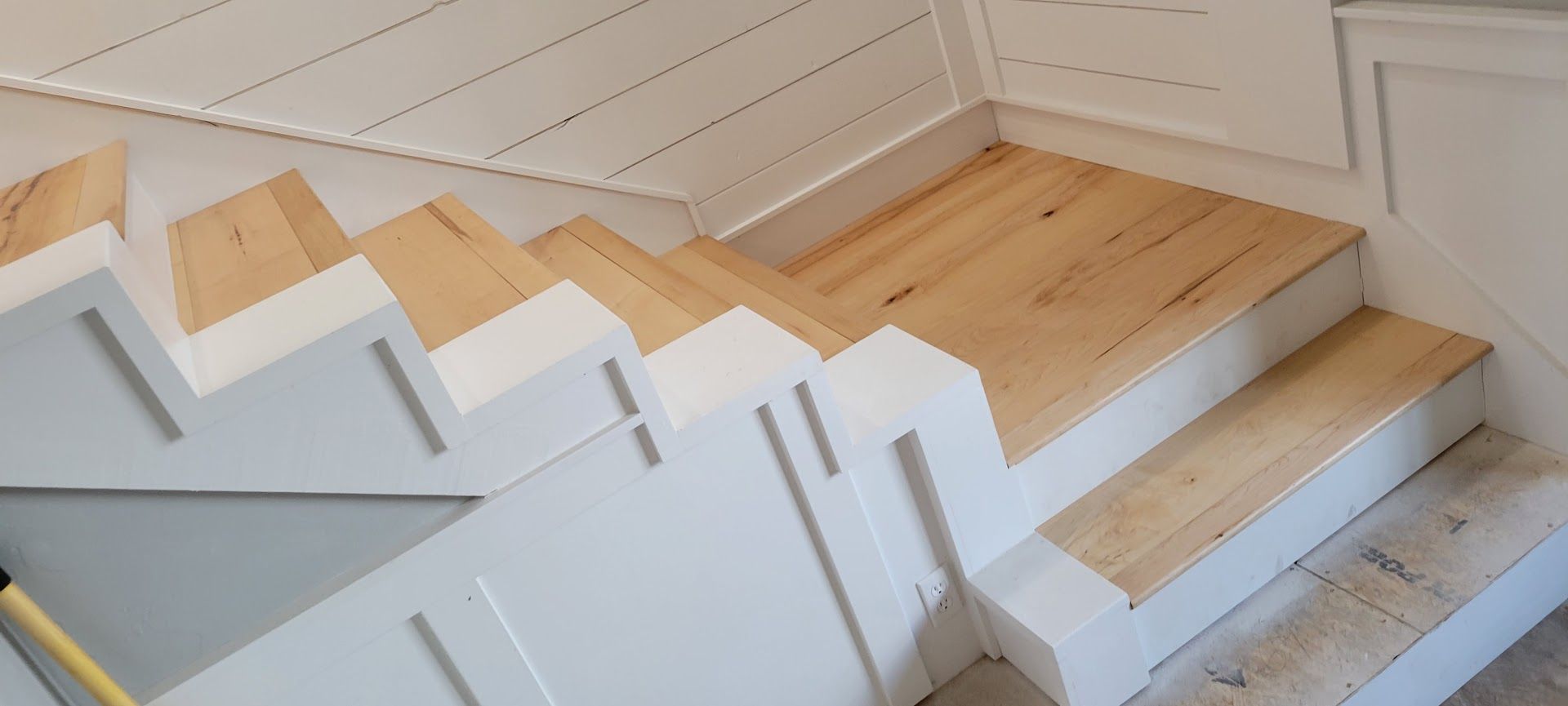 White stair railing beside light wood steps in a bright interior hallway