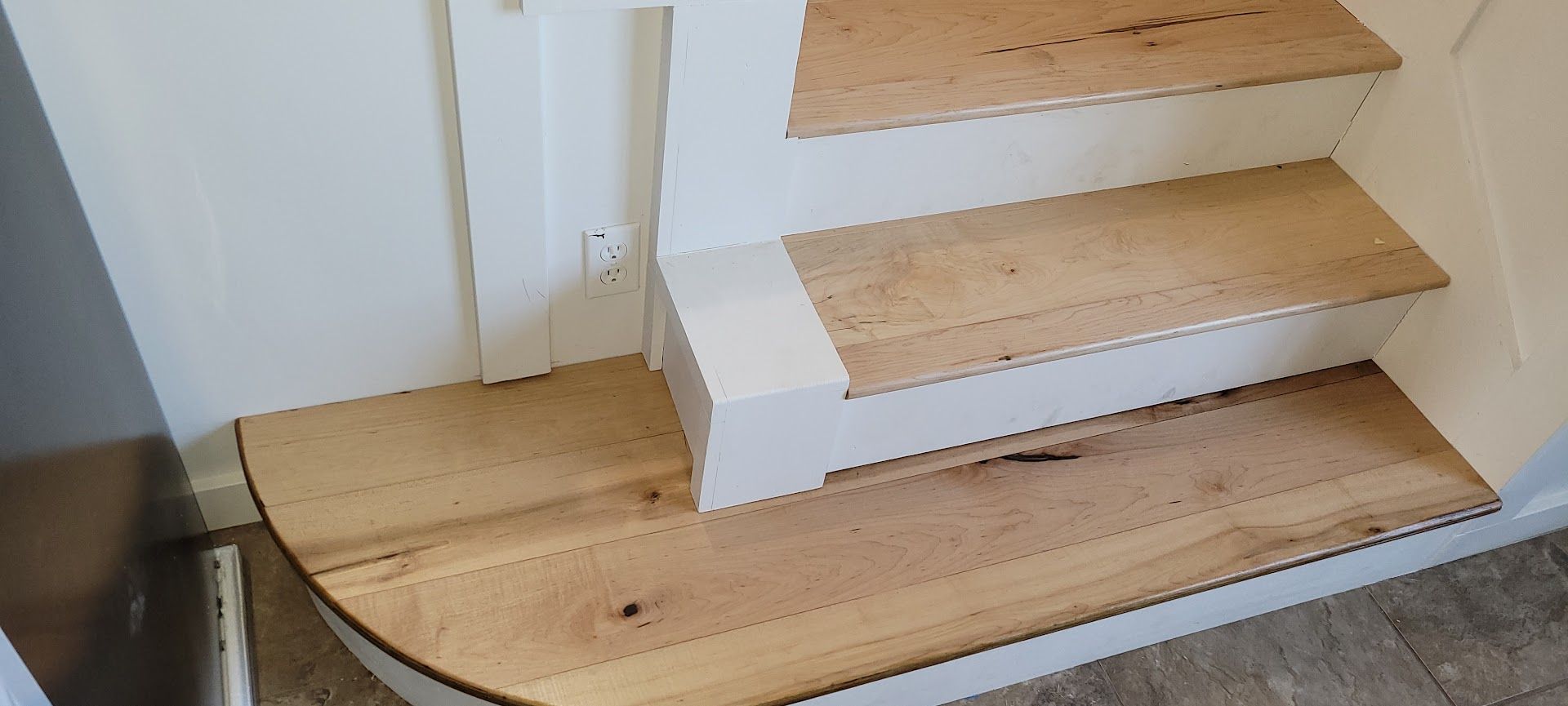 Wooden staircase with a curved bottom step and white side walls in a home interior
