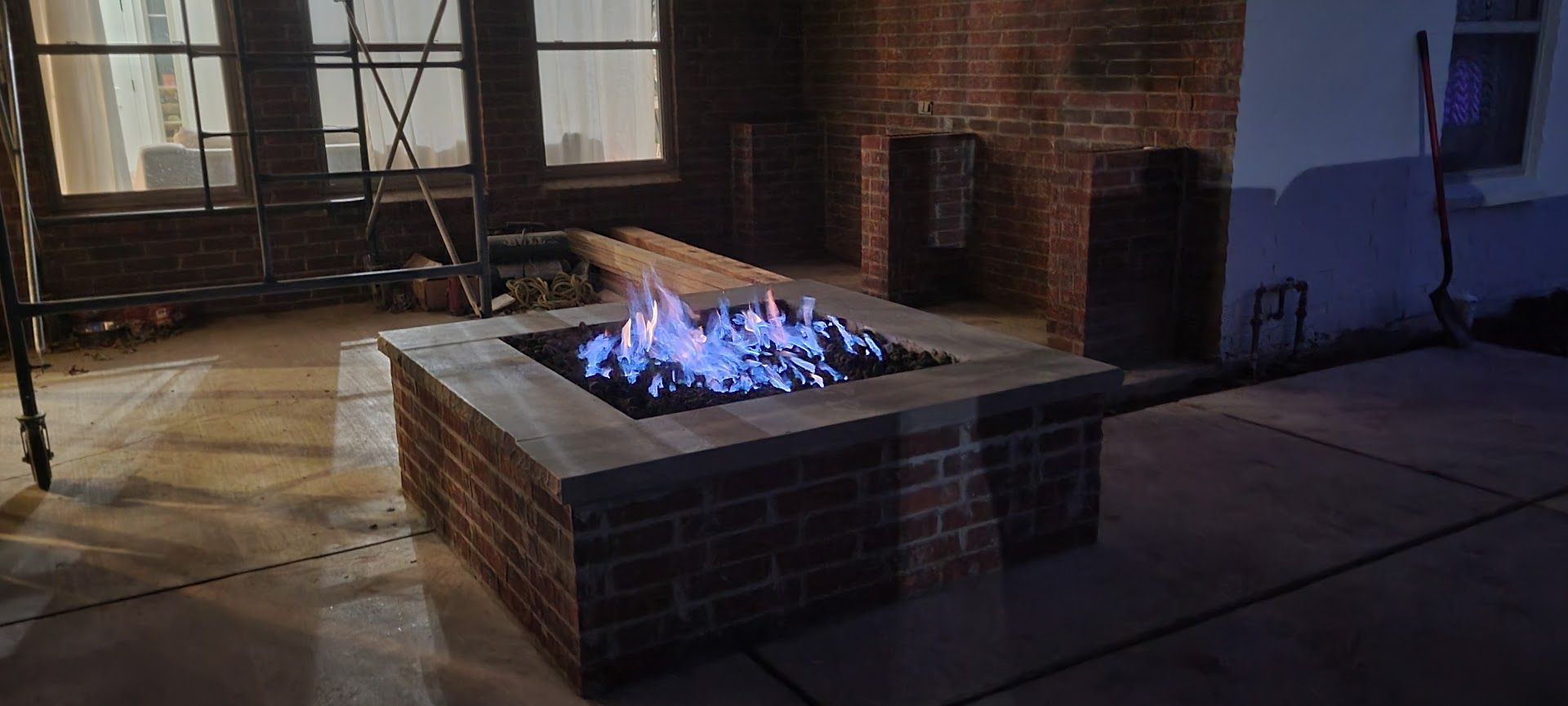 Brick fire pit with blue flames burning on a patio at night