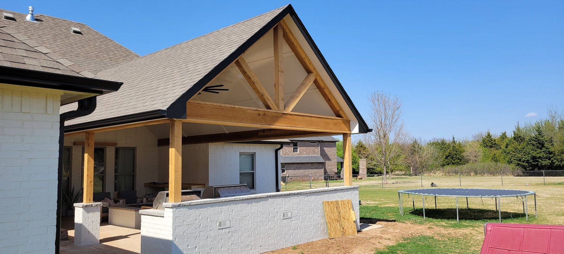 Modern house patio with wood beams, stone walls, and a grassy yard under a clear blue sky