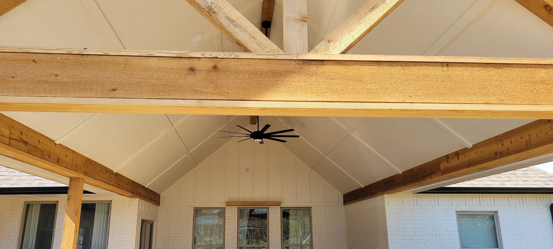 Covered patio ceiling with exposed wooden beams and a central ceiling fan above windows and sliding doors