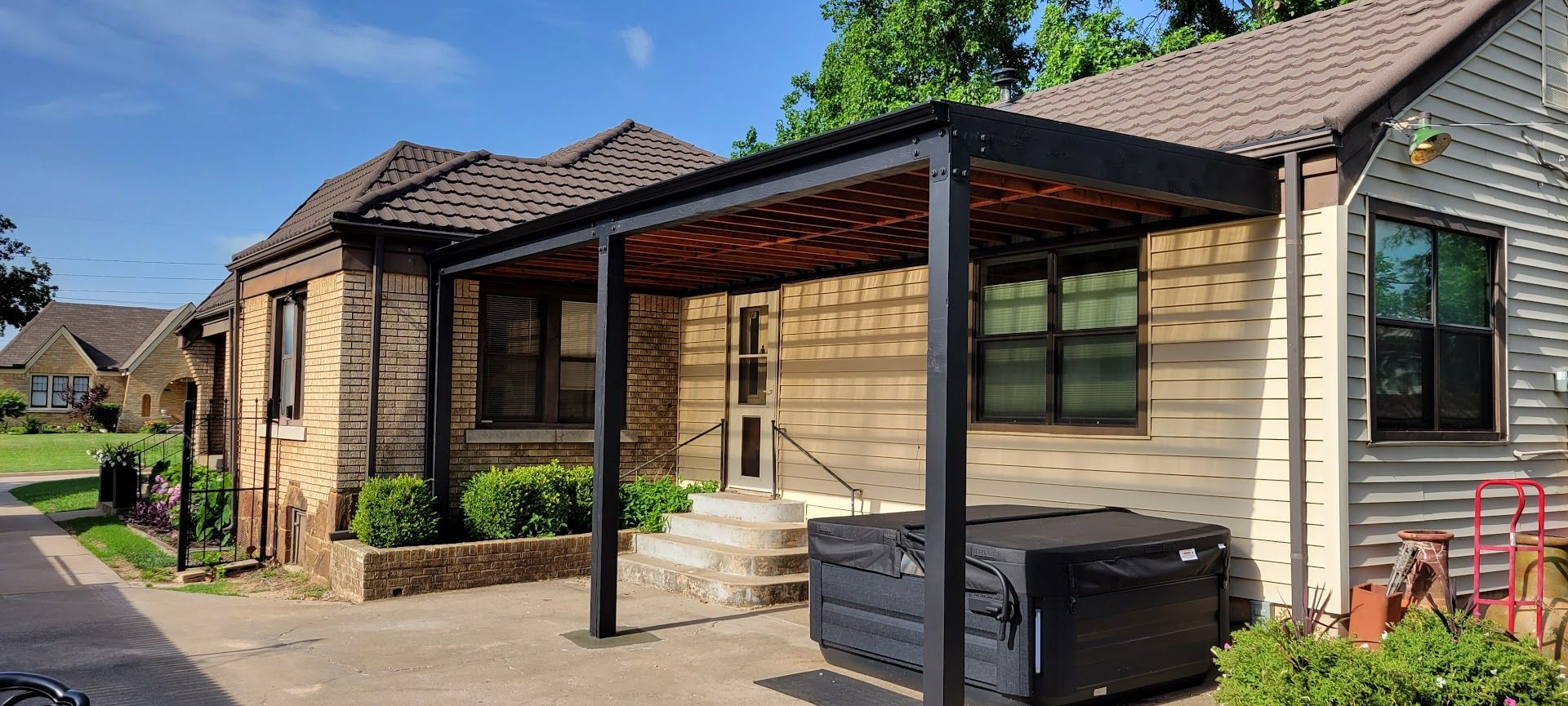 Modern single-story house with a covered patio, black pergola, and outdoor seating along a concrete walkway