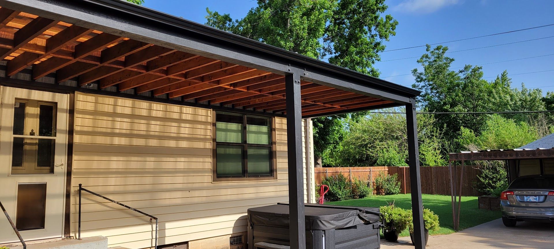 Modern house exterior with wood siding, covered patio, and parked car in a sunny yard