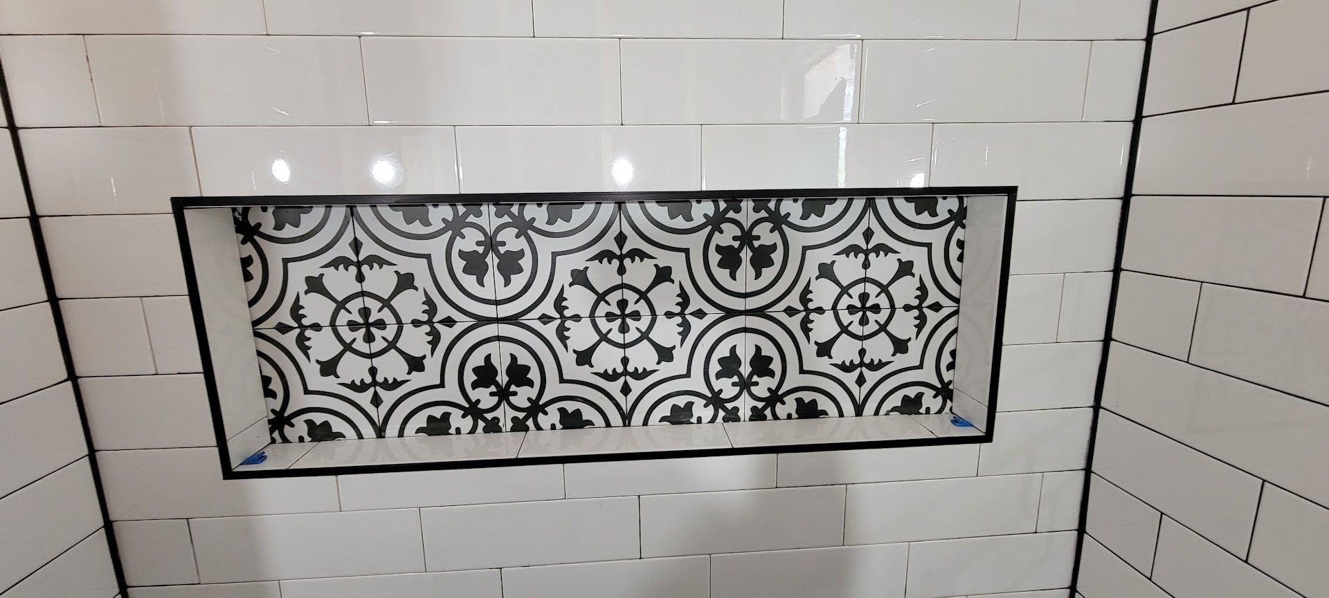 Decorative black-and-white patterned tile inset in a white subway-tiled shower wall