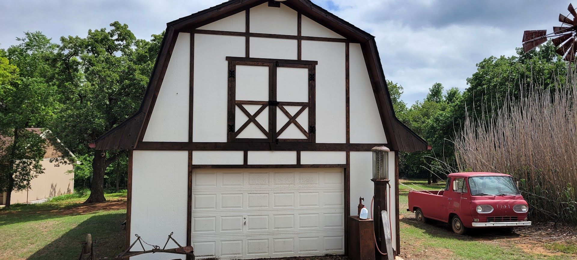 White barn-style garage with dark trim, red car parked beside it, and trees in the background