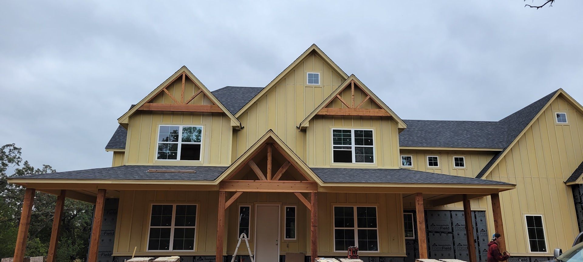 Yellow house under construction with dark roof and front porch