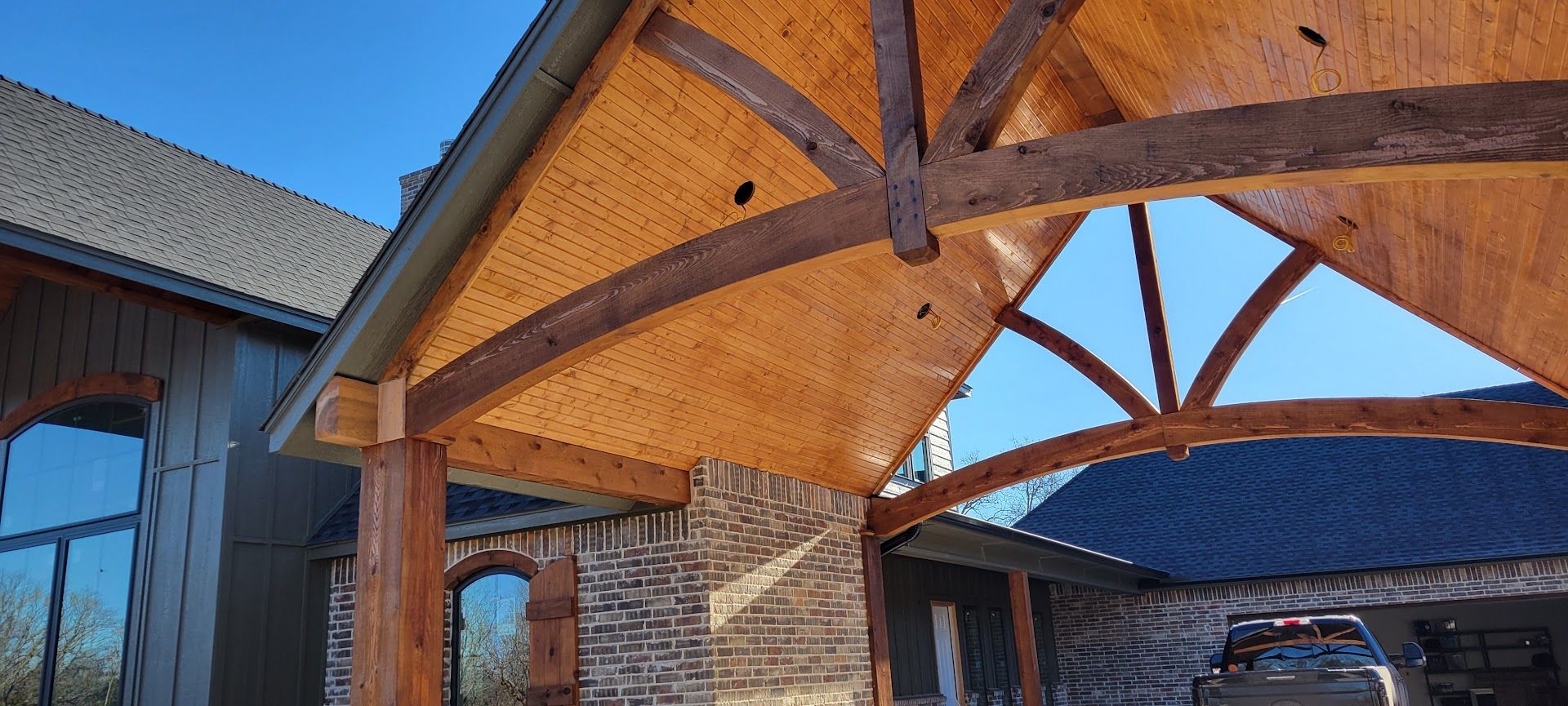 Covered driveway with wooden beams, stone pillars, and a blue metal roof at a house entrance