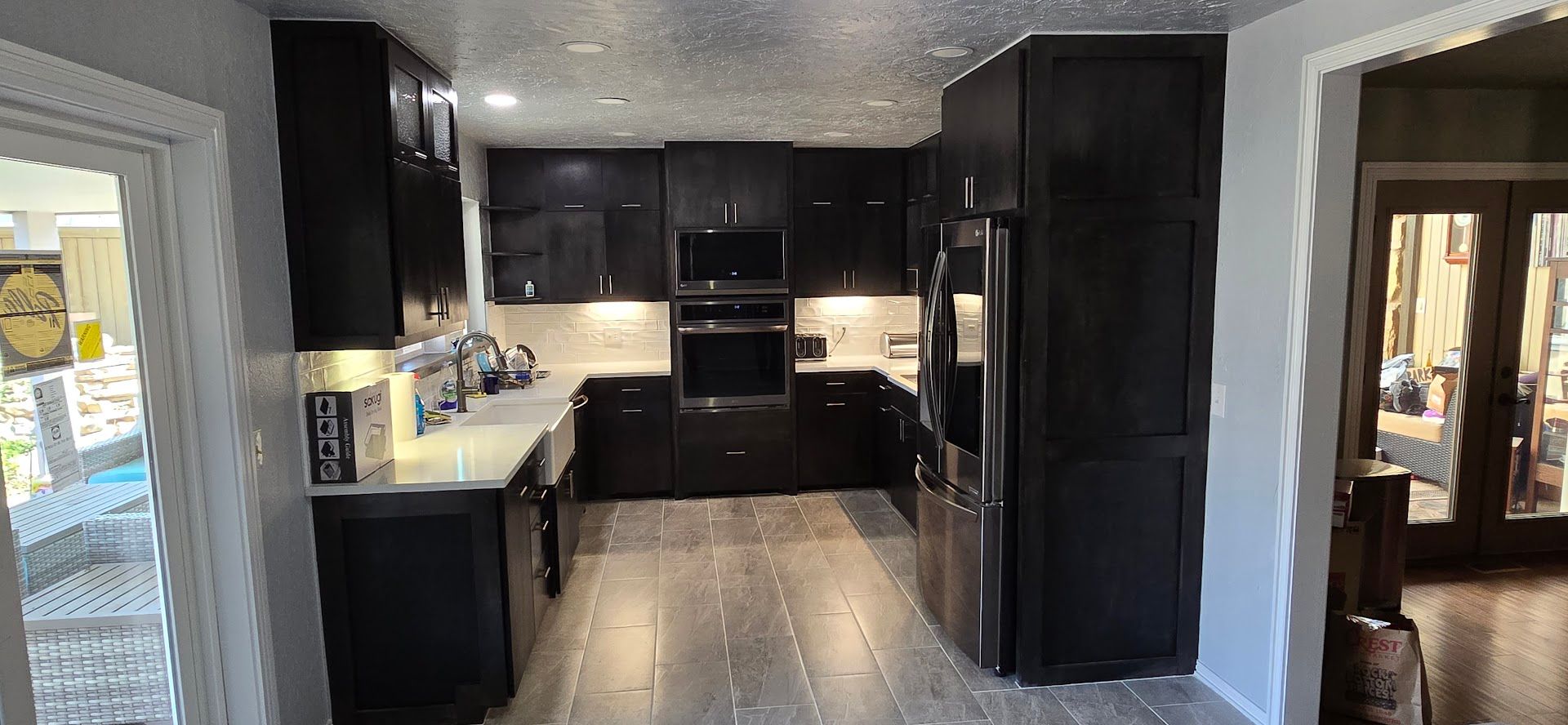 Modern black kitchen with dark cabinets, white countertops, and tile flooring, viewed from the doorway