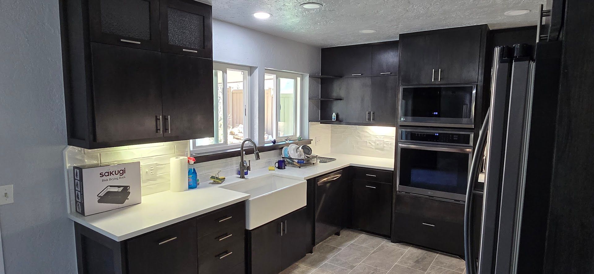 Modern kitchen with dark cabinets, stainless appliances, white counters, and a window over the sink