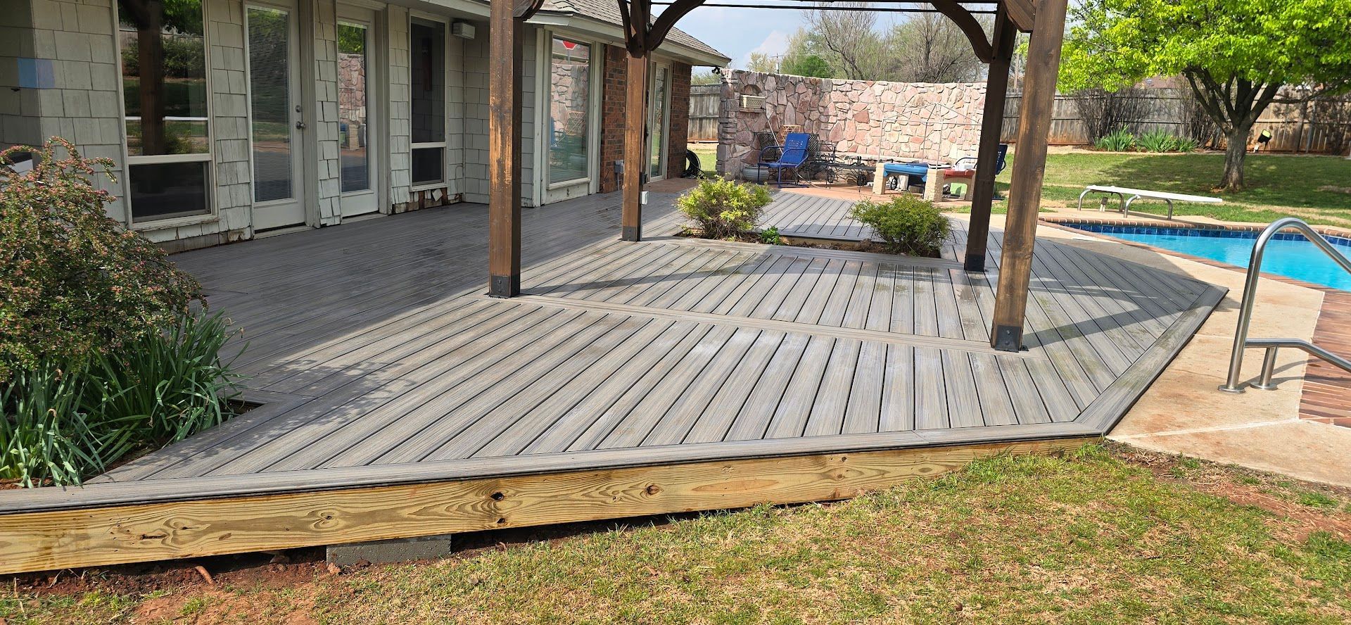 Wooden deck patio beside a house with a pool and yard in the background