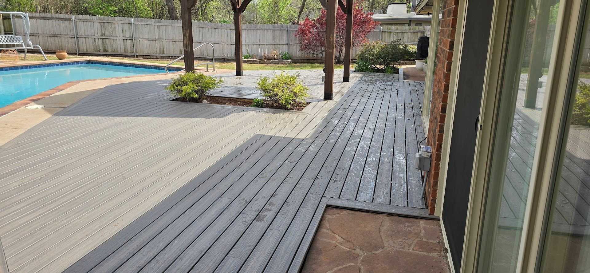 Poolside patio with gray decking, a paved walkway, and landscaping beside a building