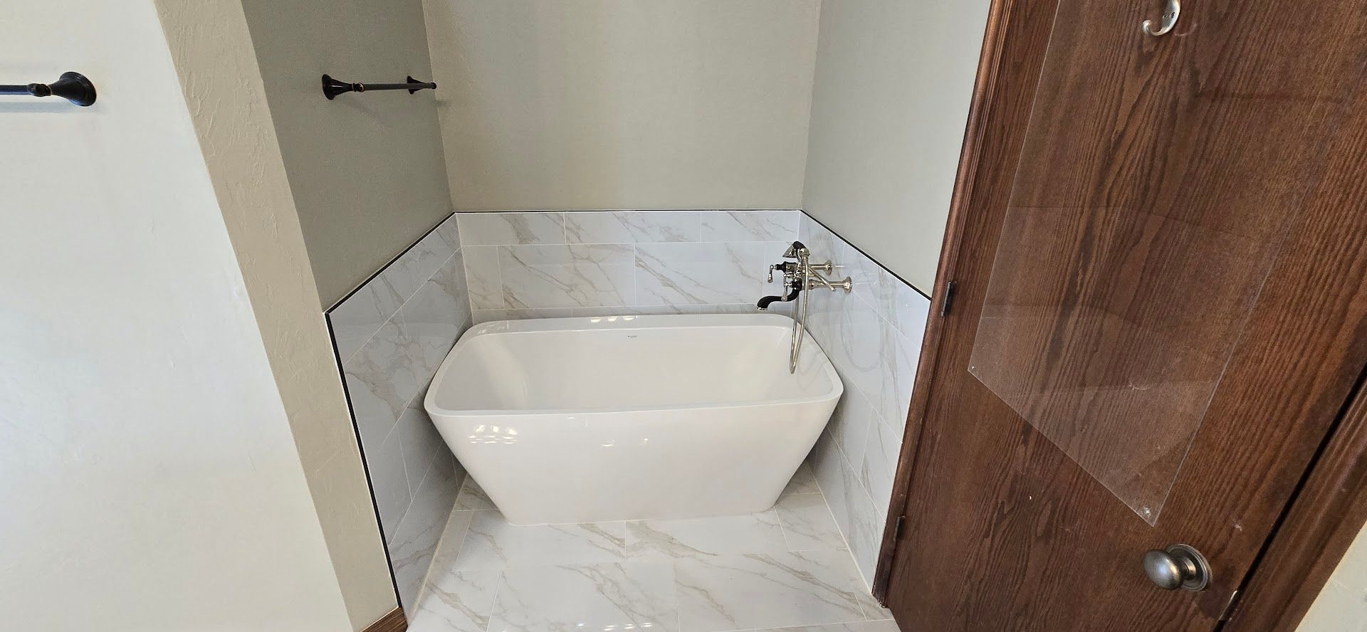 Small bathroom with a white corner sink and marble tile walls and floor, beside a wooden door.