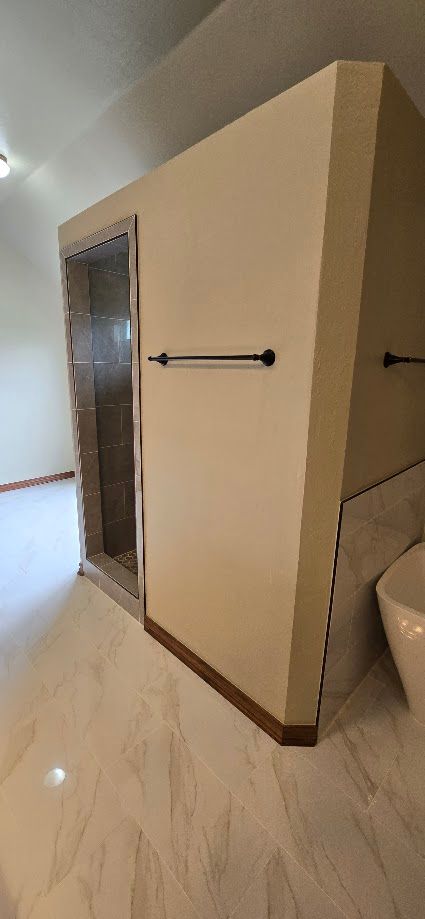 Bathroom doorway with beige walls, marble floor, towel bars, and a partially visible toilet