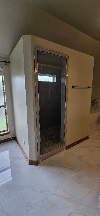 Small room with a stainless-steel sauna or steam shower enclosure beside a window and tiled floor