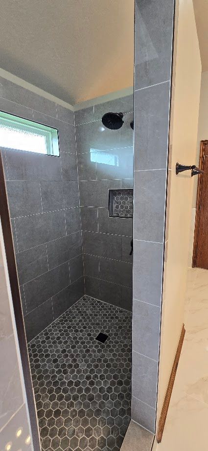 Small tiled walk-in shower with gray hexagon floor, dark wall tiles, and a small window.