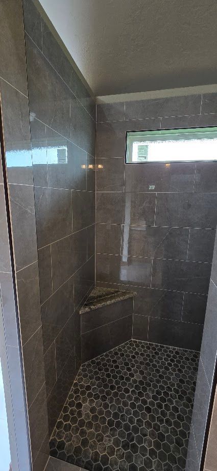 Narrow tiled shower with dark walls, hexagonal floor tile, and a small window opening for light