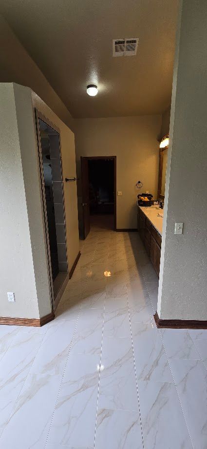 Narrow hallway with white marble floor, ceiling lights, and a dark doorway at the end