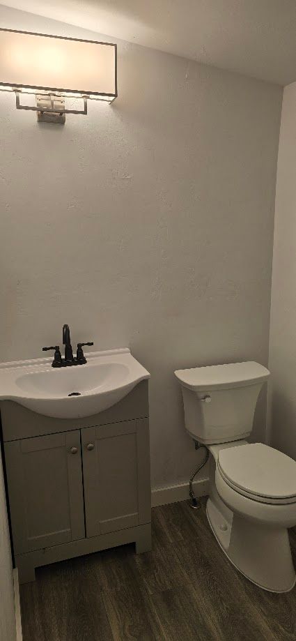 Small bathroom with white sink, toilet, and wall light on a gray wood floor.